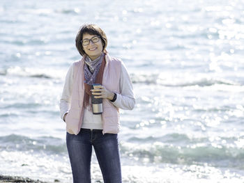 Smiling woman walking on seaside with travel mug. vacation on ocean coast. turquoise water.