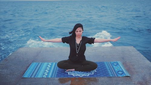 Full length of woman performing yoga against sea