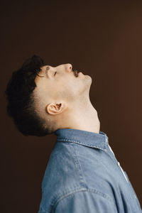 Side view of young man by brown background