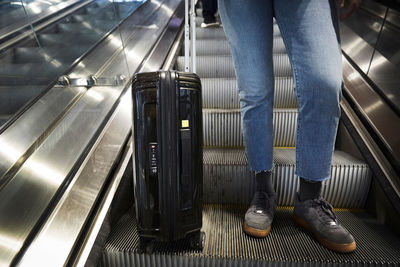 Low section of woman with wheeled suitcase standing on escalator at underground station