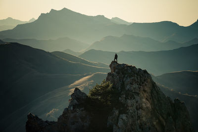 Silhouette person on rock by mountains against sky