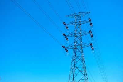 Low angle view of electricity pylon against clear blue sky