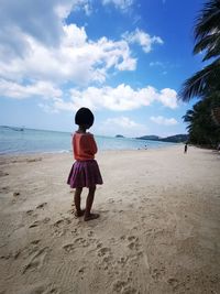 Rear view of young woman standing at beach against sky