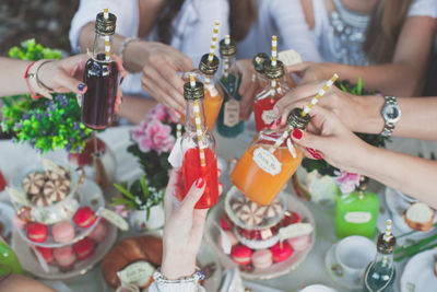 Cropped image of hands cheersing colorful drinks over macarons at a party