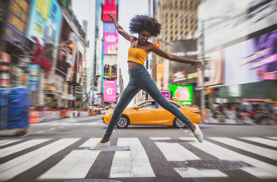 Full length of excited young woman dancing on zebra crossing in city