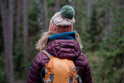 Back of a woman standing in a forest in winter hiking with a backpack