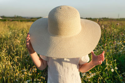 Rear view of woman wearing hat standing on field