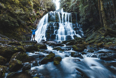 Rear view of hiker with arms outstretched looking at waterfall in forest