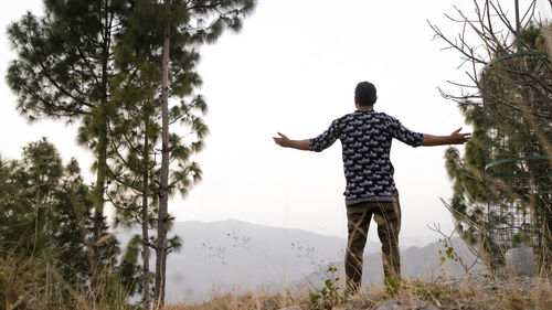 Rear view of man standing by tree against sky