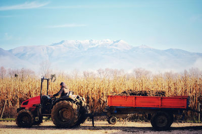 Man working with a tractor on a corn field against sky