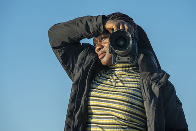Low angle view of woman with camera against clear sky