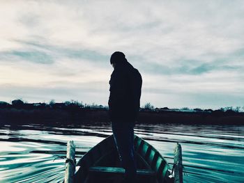 Rear view of silhouette man standing by lake against sky