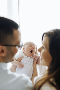 Mom and dad from behind holding their newborn baby son yawning. new parents