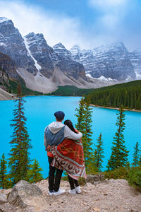 Rear view of man standing by lake against mountains