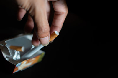 Cropped hand of person holding pills against black background