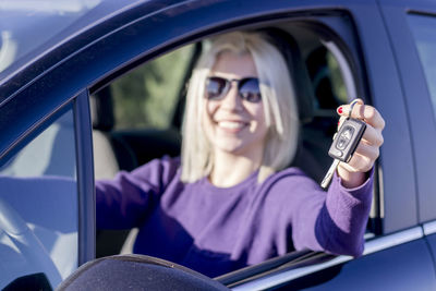 Portrait of smiling woman holding key while sitting in car