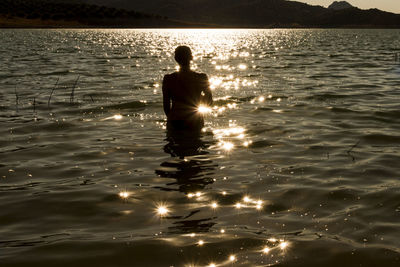 Silhouette man in sea against sky during sunset