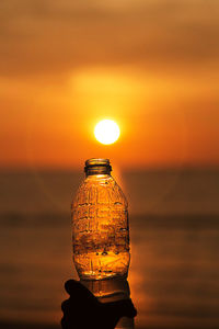 Man holding bottle against orange sunset sky