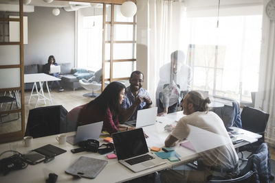 Male and female coworkers discussing in meeting at creative office seen through glass wall