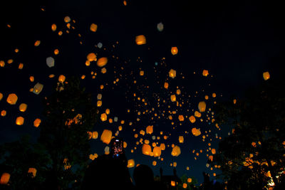 Low angle view of illuminated paper lanterns flying in sky at night