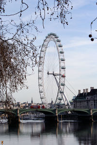 Ferris wheel by river against sky in city