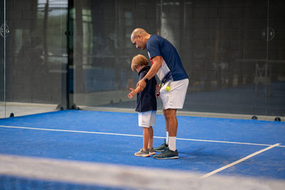 Monitor teaching padel class to child, his student - trainer teaches little boy how to play padel 
