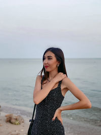 Young woman standing at beach against sky