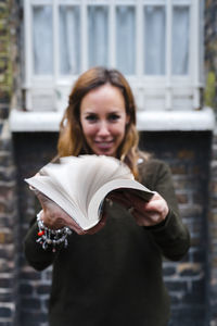 Portrait of a smiling young woman holding camera outdoors