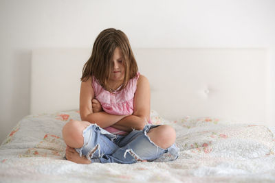 Girl child serious and frustrated sitting on a bed in a bright bedroom, concept age crisis 