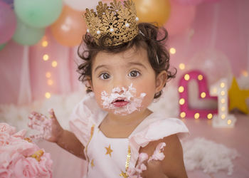 Cute baby girl with balloons and birthday cake sitting at home