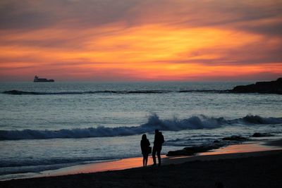 Silhouette people standing at beach against sky during sunset