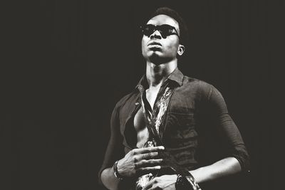 Portrait of young man in sunglasses standing against black background