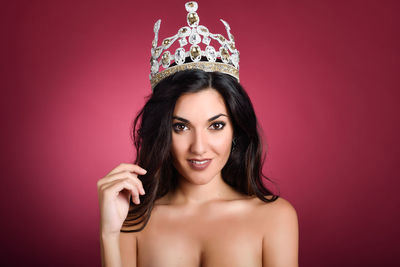 Portrait of shirtless beautiful model wearing crown against red background
