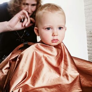 Female hairdresser cutting baby boy hair at hair salon