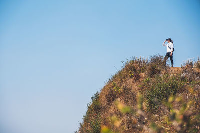 Man standing by tree against clear blue sky