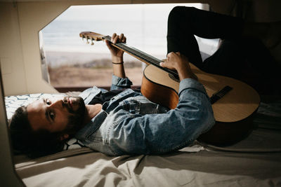 Man playing guitar while lying down on bed