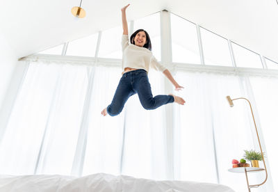 Full length of young woman jumping on bed at home