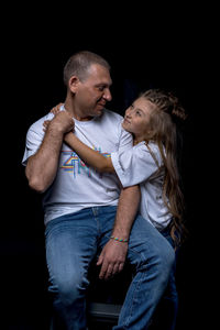 Full length of father with daughter against black background