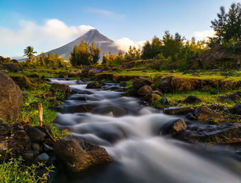 Scenic view of stream flowing through rocks against sky
