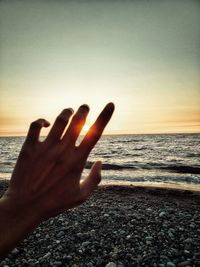 Close-up of hand on sand at beach against sky