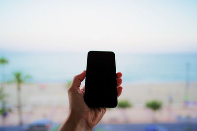 Close-up of mans hand photographing sea against sky