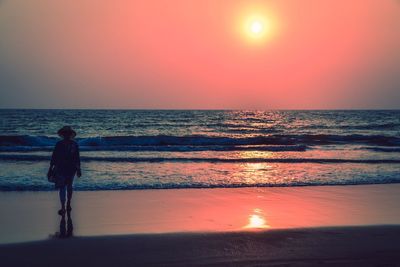 Rear view of man standing at beach during sunset