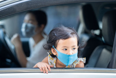 Mother and daughter wearing medical disposable face mask while parking a car.