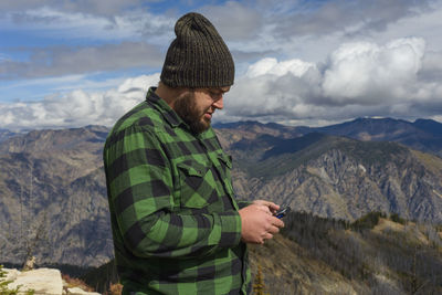 Male in flannel with cell phone on mountain top