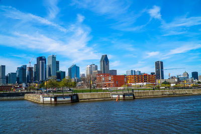 City skyline by river against blue sky