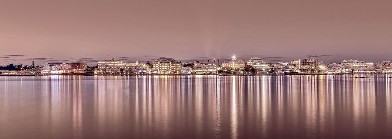 Illuminated buildings by sea against sky at night