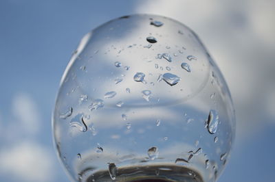 Close-up of water drops on glass against sky