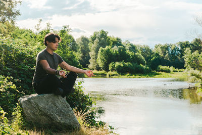 Full length of man sitting by lake against sky