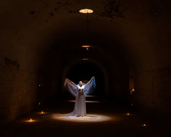 Lady in white bride dress like an angel at a religious mass with burning torches in the dungeon