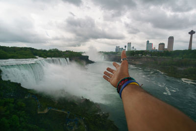 Cropped hand of man reaching towards against niagara falls